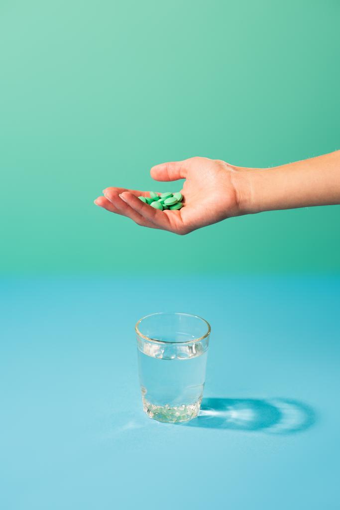 oříznuté shot osoby držící prášky nad sklenicí vody na zelené - Fotografie, Obrázek