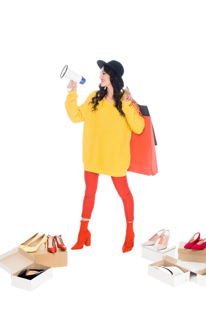 hermosa mujer joven sosteniendo megáfono y bolsas de compras aisladas en blanco con zapatos
 - Foto, imagen