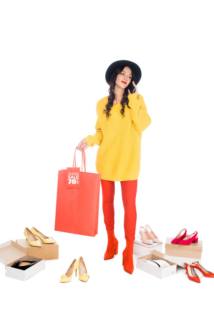 mulher bonita falando no smartphone e segurando saco de compras com etiqueta de venda isolada no branco com caixas de calçados
 - Foto, Imagem
