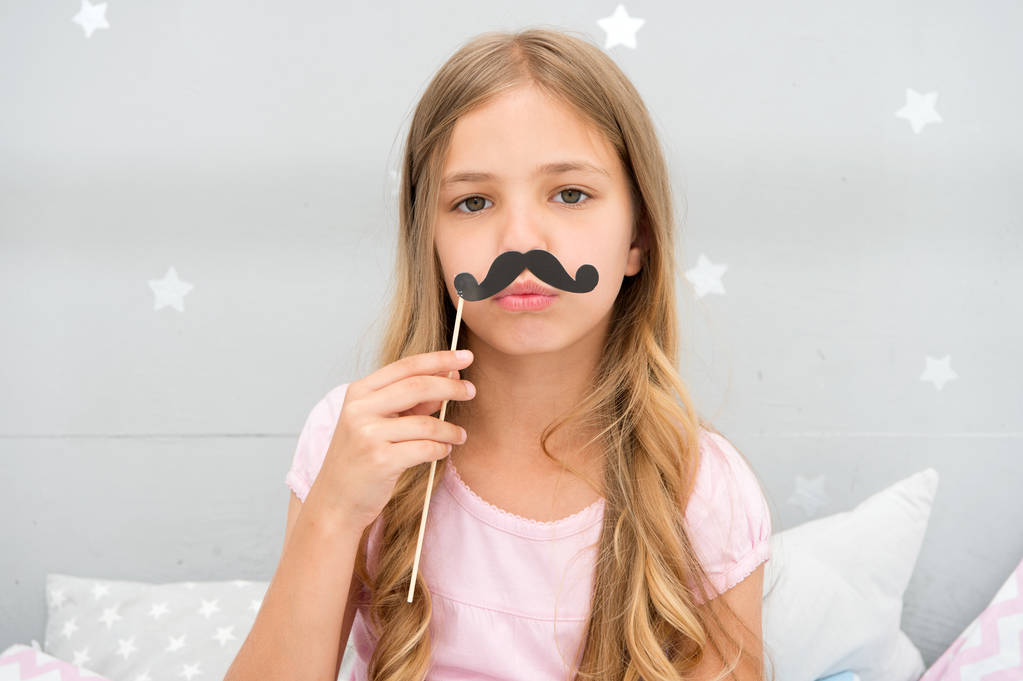 Pajamas party concept. Girl fake mustache at pajamas party. Cheerful kid posing mustache. Photo booth props ideas. Printable accessories for party. Girl long blonde hair posing with photo booth props - Photo, Image