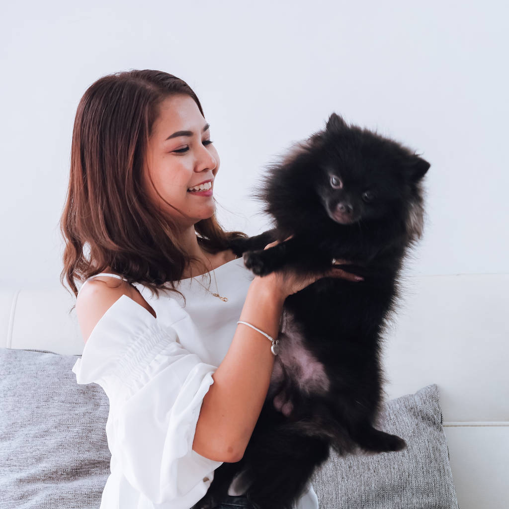 Boldog ázsiai nő játszik a kanapén, otthon, fekete kutyájával életmód fogalma - Fotó, kép