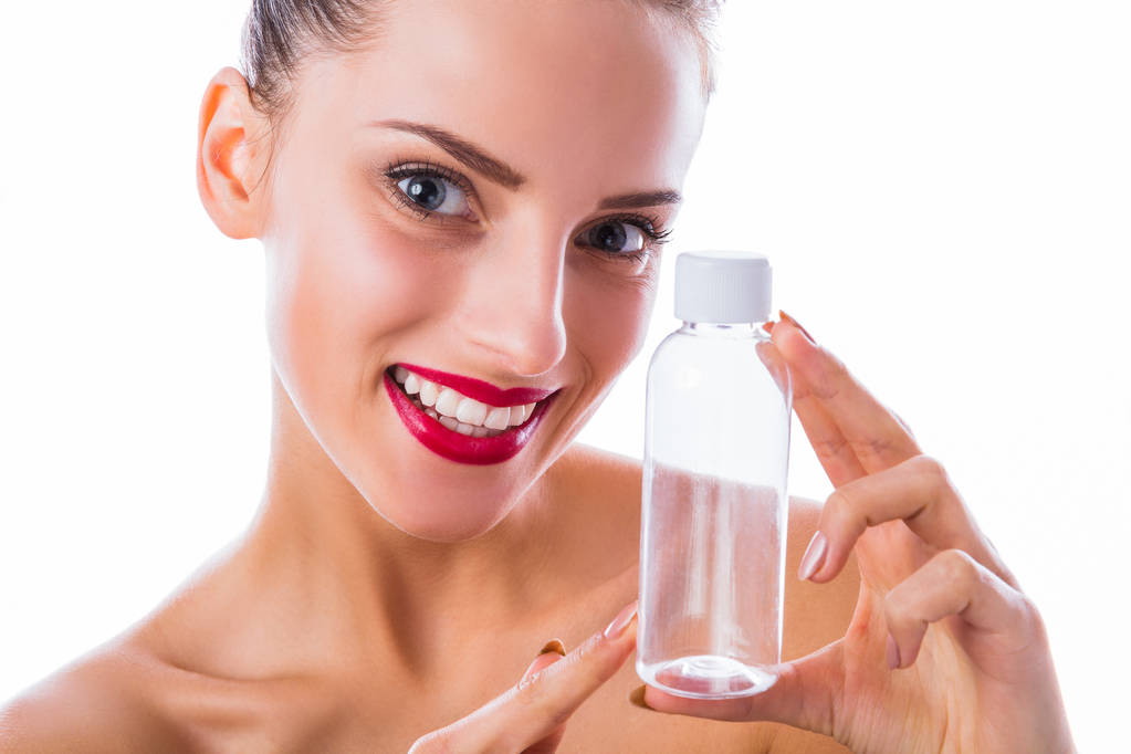 Close-up maravilhoso, mulher sorridente mantém garrafa vazia na mão perto de seu rosto no fundo branco
 - Foto, Imagem