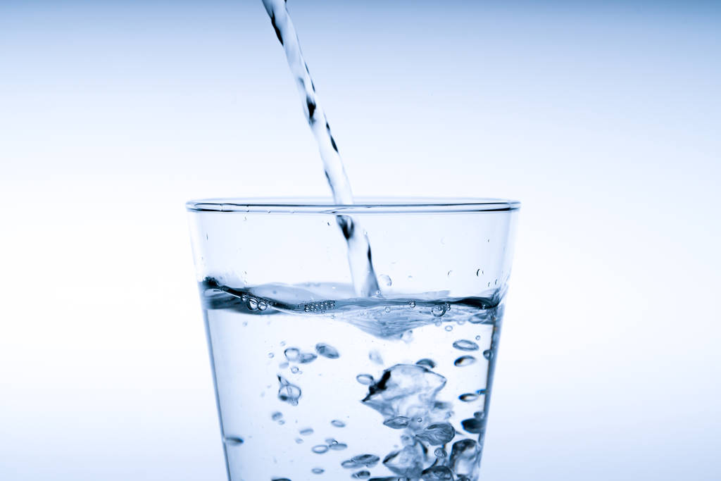 Close-up van gieten drinkwater in glas, studio opname - Foto, afbeelding