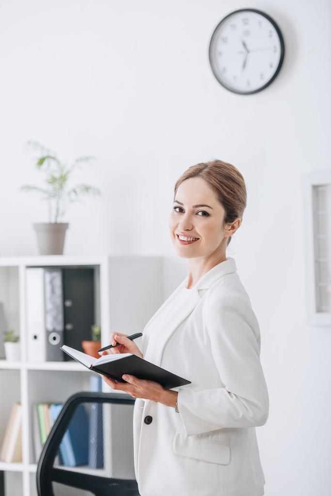 atrakcyjna kobieta interesu uśmiechający się pracę z planner w nowoczesnym biurze - Zdjęcie, obraz