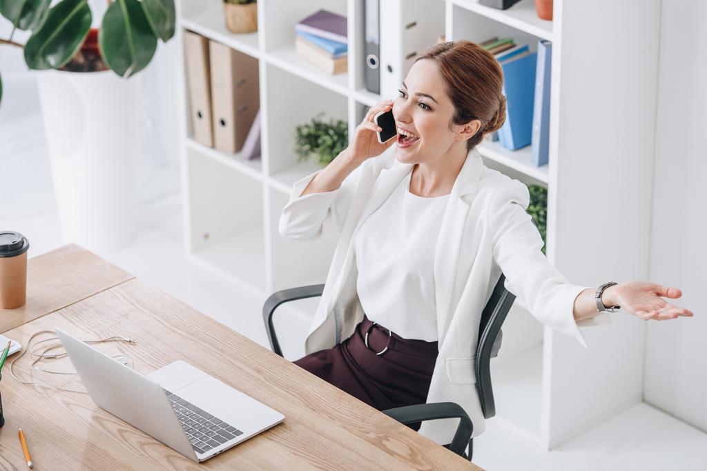 donna d'affari eccitata che parla su smartphone in ufficio moderno con computer portatile
 - Foto, immagini