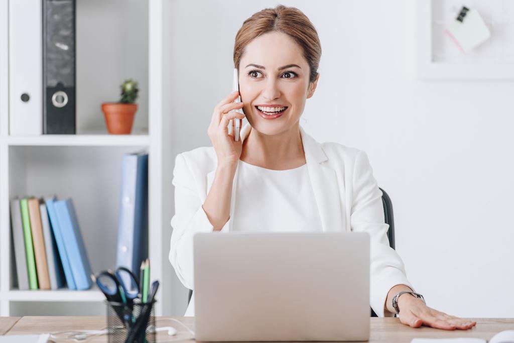 exitosa mujer de negocios hablando en el teléfono inteligente y el uso de ordenador portátil en el lugar de trabajo
 - Foto, imagen