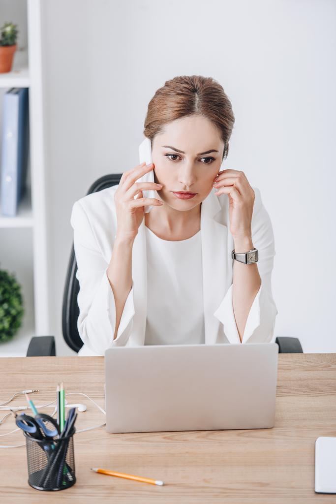 donna d'affari stressata che parla su smartphone sul posto di lavoro con il computer portatile
  - Foto, immagini