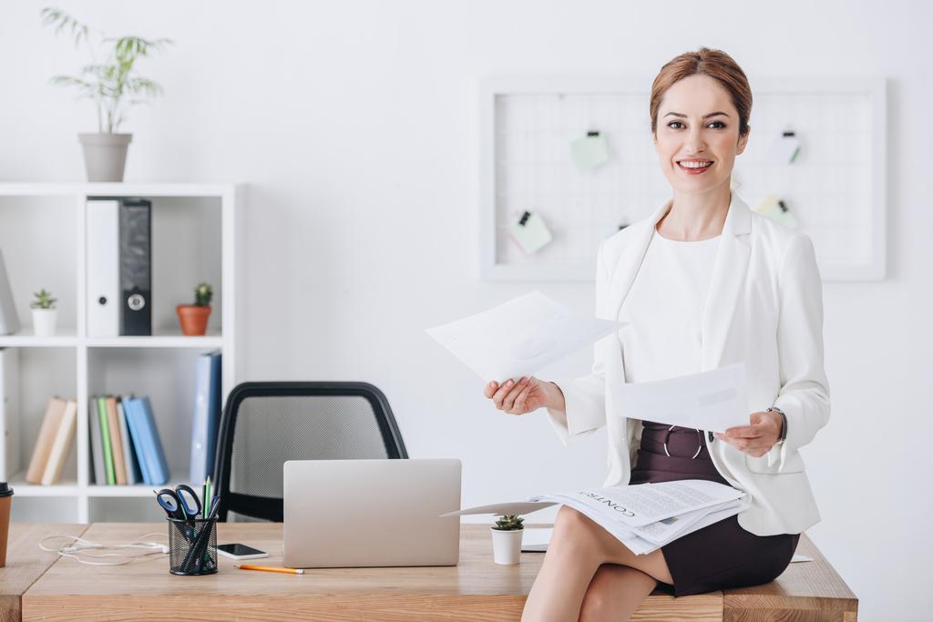 executive businesswoman doing paperwork while sitting on table with laptop - Photo, Image