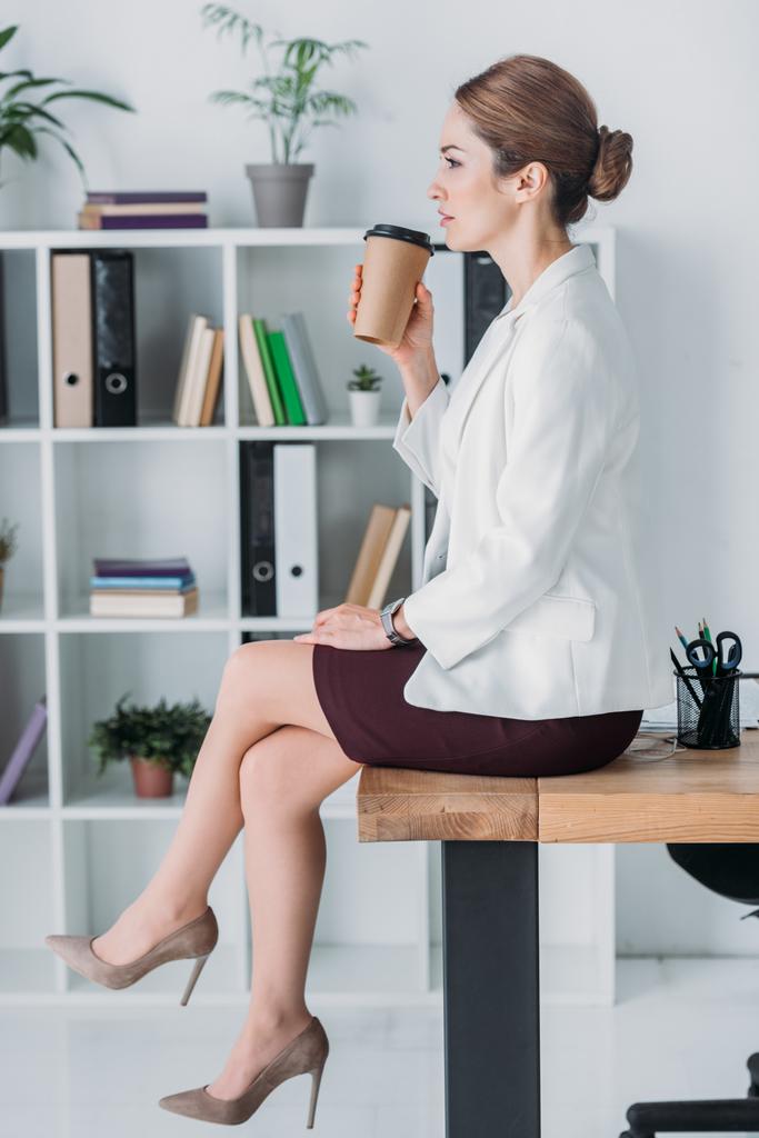 бізнес-леді з паперовою чашкою, що сидить на столі під час кавової перерви в офісі
 - Фото, зображення