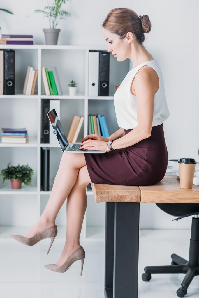 mulher de negócios atraente que trabalha com laptop enquanto está sentado na mesa no escritório
 - Foto, Imagem