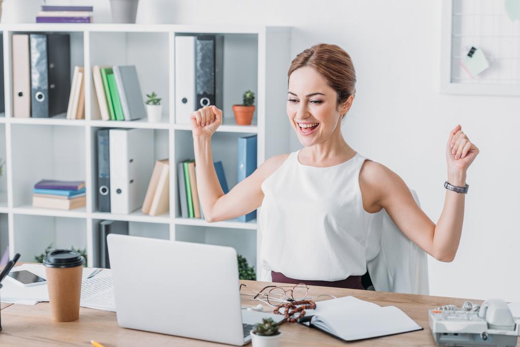 Erfolgreiche Geschäftsfrau feiert am Arbeitsplatz und blickt auf Laptop - Foto, Bild