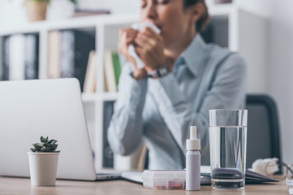 лекарства, стоящие на рабочем столе с размытой чихающей бизнес-леди, сидящей на заднем плане
 - Фото, изображение