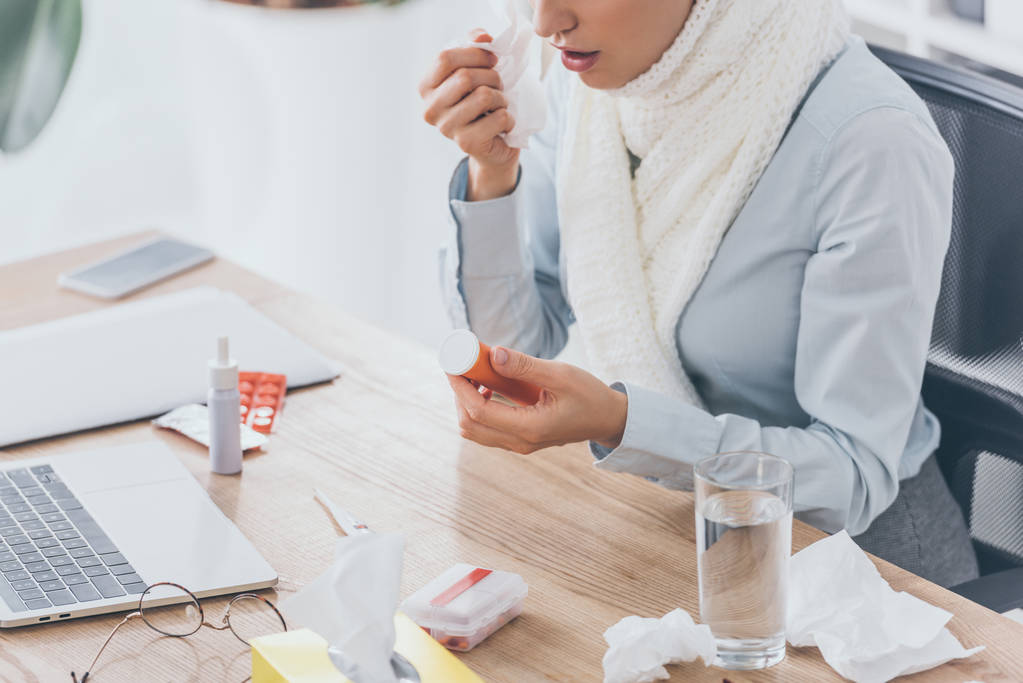 bijgesneden schot van zieke zakenvrouw in sjaal container van pillen houden op werkplek - Foto, afbeelding