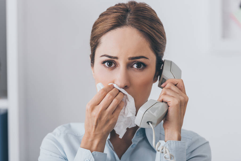 close-up portrait of businesswoman with runny nose talking by wired phone and looking at camera - Photo, Image