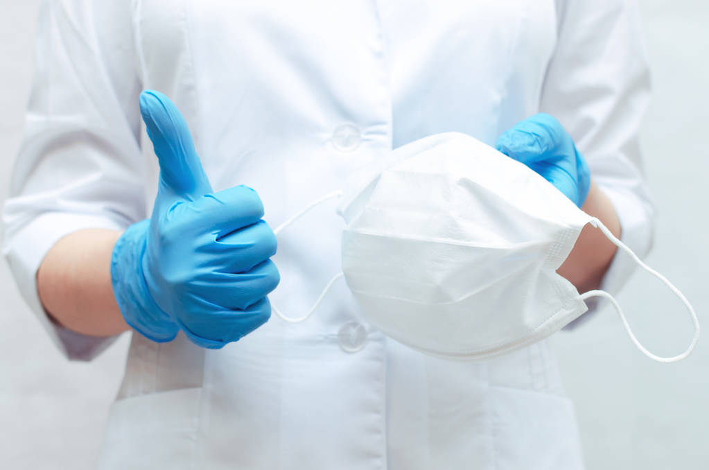 Медична маска в руках лікаря, одягнена в блакитні медичні рукавички. Використовувати медичну маску для запобігання захворюванню
. - Фото, зображення