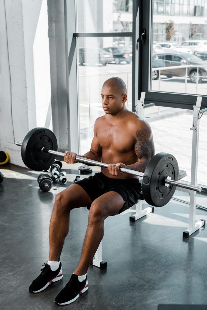 high angle view of athletic young african american sportsman sitting on bench and lifting barbell in gym - Photo, Image