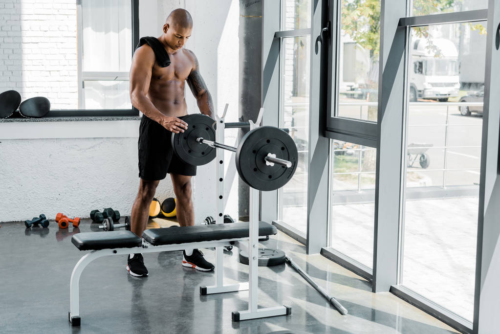 мускулистый молодой спортсмен с полотенцем тренировки с штангой в тренажерном зале
 - Фото, изображение