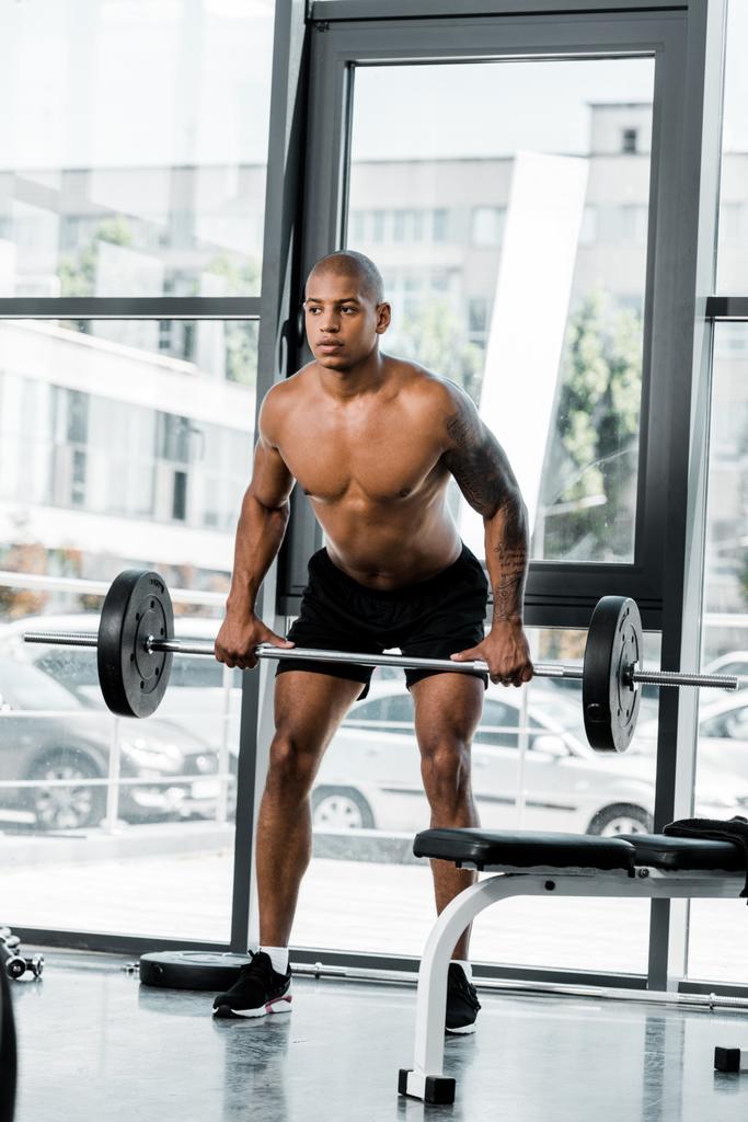 visão de comprimento total de muscular shirtless jovem desportista levantando barbell no ginásio
 - Foto, Imagem