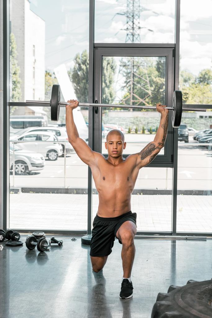 muskulöser junger Sportler mit nacktem Oberkörper beim Hantelheben im Fitnessstudio  - Foto, Bild