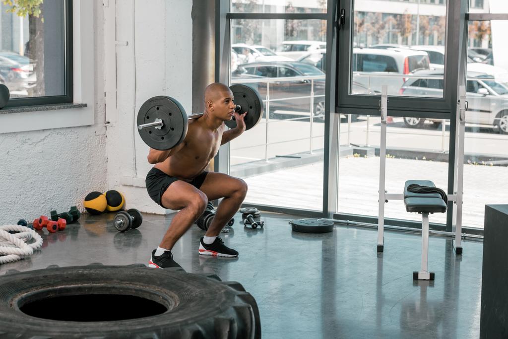 young muscular african american man lifting barbell and looking away in gym - Photo, Image
