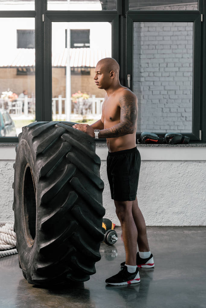 вид сбоку на мускулистого молодого человека, тренирующегося с шиной и смотрящего в спортзале
 - Фото, изображение