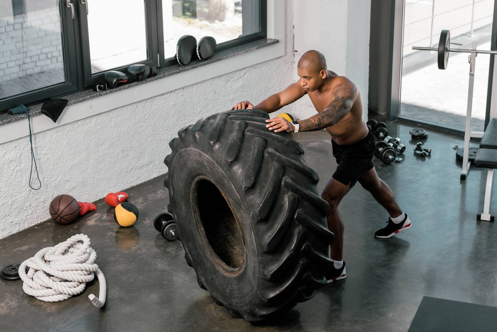 alto ángulo vista de muscular joven afroamericano hombre entrenamiento con neumático en gimnasio
 - Foto, imagen