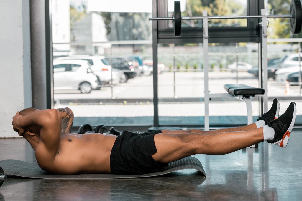 επιλεκτική εστίαση της αφρικανική αμερικανική άνθρωπος που κάνει abs σε ματ γυμναστηρίου στο γυμναστήριο - Φωτογραφία, εικόνα