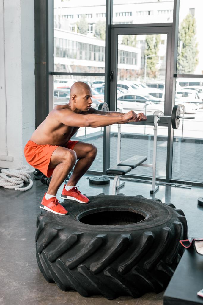 gömleksiz Afro-Amerikan atlet lastik spor salonunda egzersiz yaparken yan görünüm - Fotoğraf, Görsel