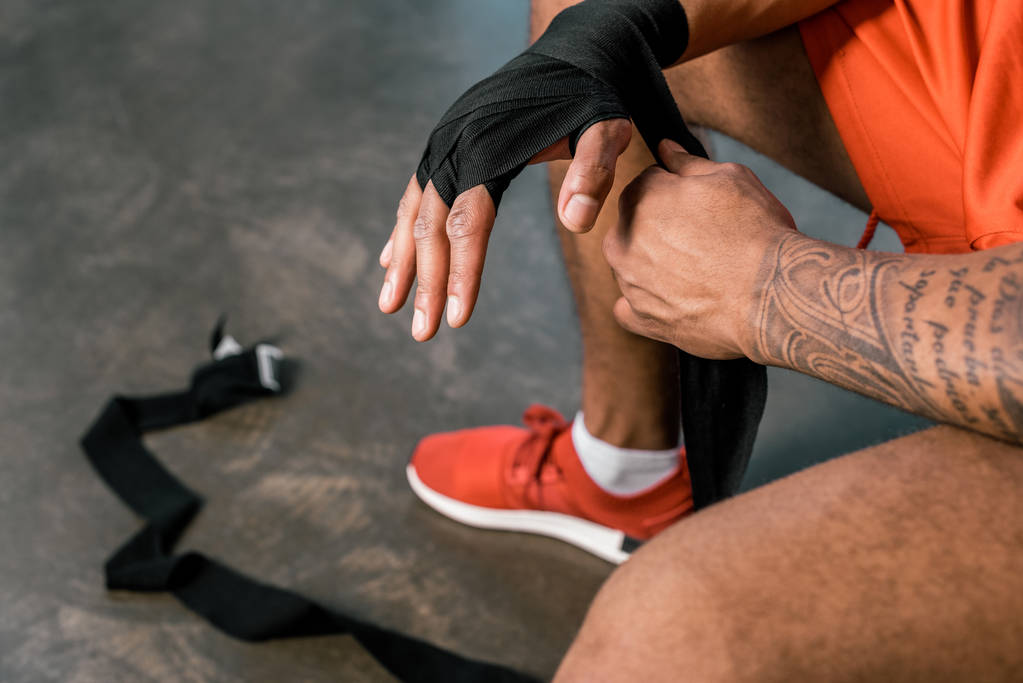 visão parcial de tatuado desportista afro-americano envolvendo mão em bandagem de boxe no ginásio
 - Foto, Imagem
