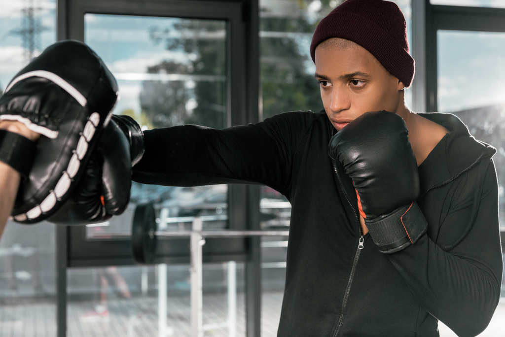 jovem pugilista afro-americano em luvas de boxe praticando com treinador no ginásio
 - Foto, Imagem