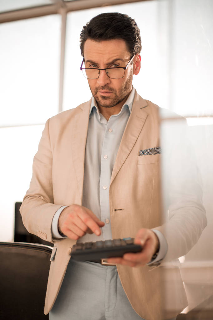 hombre de negocios serio usando una calculadora mientras está de pie en la oficina vacía - Foto, imagen