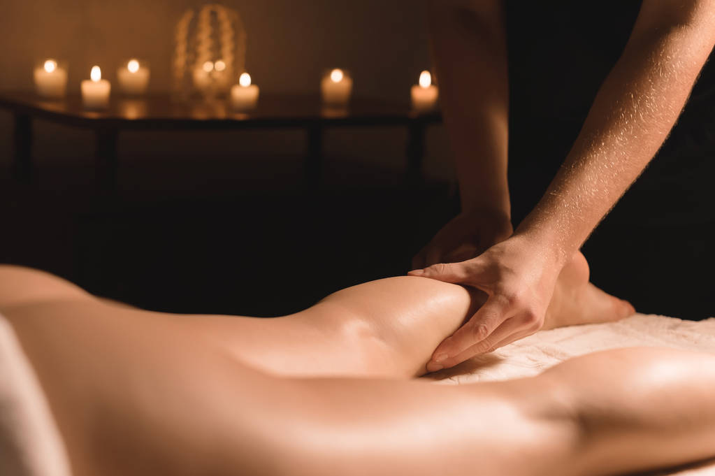 Szczelnie-do góry ręce mężczyzna robi masaż łydek, kobiece nogi w ciemnym pokoju ze świecami w tle. Zabiegów kosmetycznych i spa - Zdjęcie, obraz