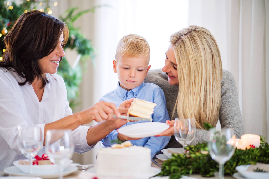 Маленький мальчик с мамой и бабушкой едят торт на Рождество
. - Фото, изображение