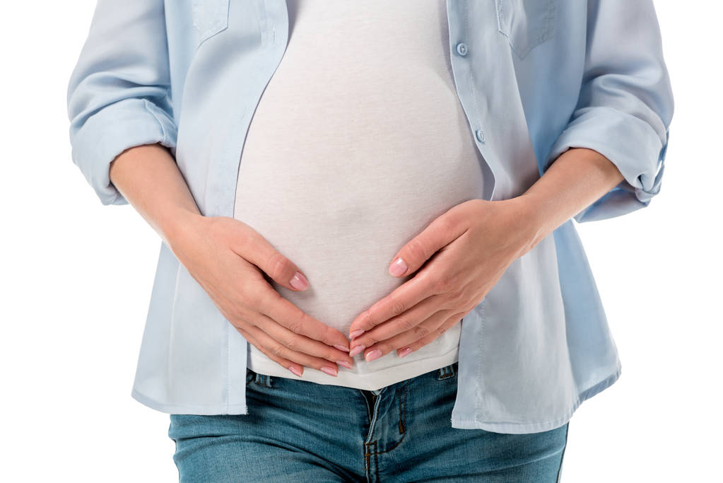 Schnappschuss einer schwangeren Frau in Jeans und Hemd, die den Bauch hält und die Hände isoliert auf weiß hält - Foto, Bild