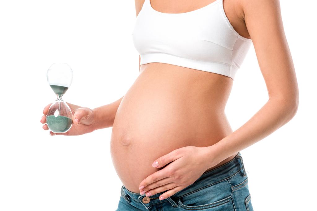 vue recadrée de la femme enceinte touchant le ventre et tenant sablier isolé sur blanc
 - Photo, image