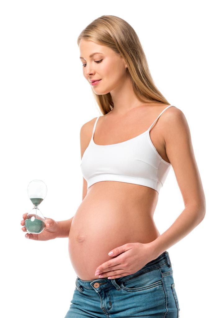 όμορφη έγκυος γυναίκα κρατώντας κλεψύδρα που απομονώνονται σε λευκό - Φωτογραφία, εικόνα