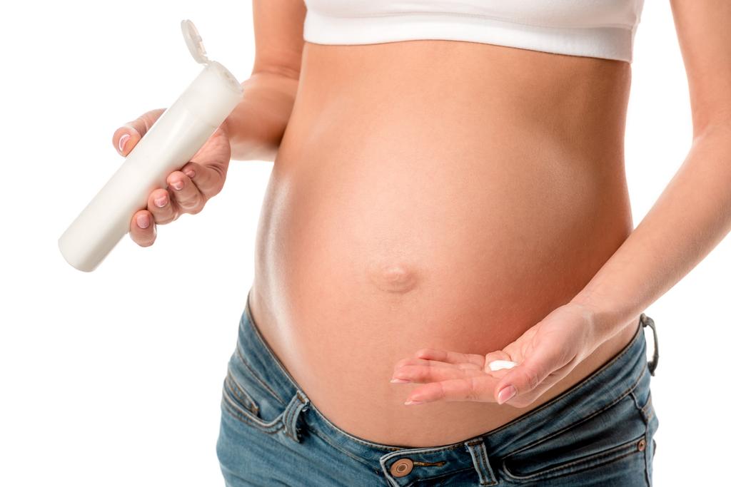 Kırpılan görünümü üzerinde beyaz izole çatlakları önlemek için hamile kadının karın üzerinde kozmetik losyon uygulamak - Fotoğraf, Görsel