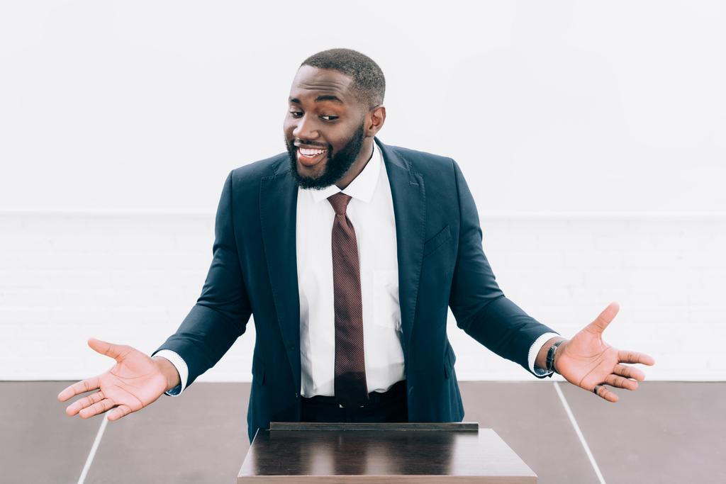 vysoký úhel pohled s úsměvem africké americké přednášející ukazující pokrčení gesto na pódium tribune v konferenčním sále - Fotografie, Obrázek