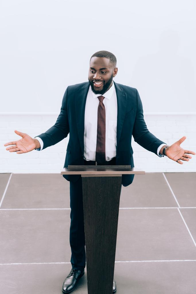 会議ホールでセミナー中に表彰台トリビューンで身振りで示すアフリカ系アメリカ人講師の笑顔ハイアングル - 写真・画像