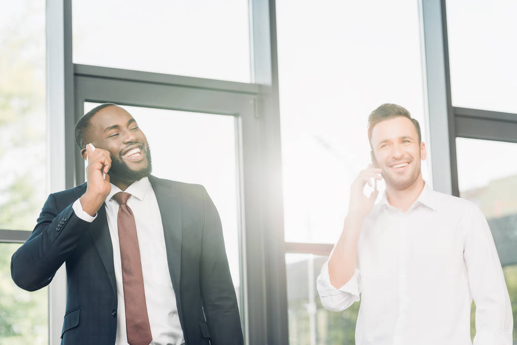 Lächelnde multikulturelle Geschäftsleute, die im Büro auf dem Smartphone sprechen - Foto, Bild