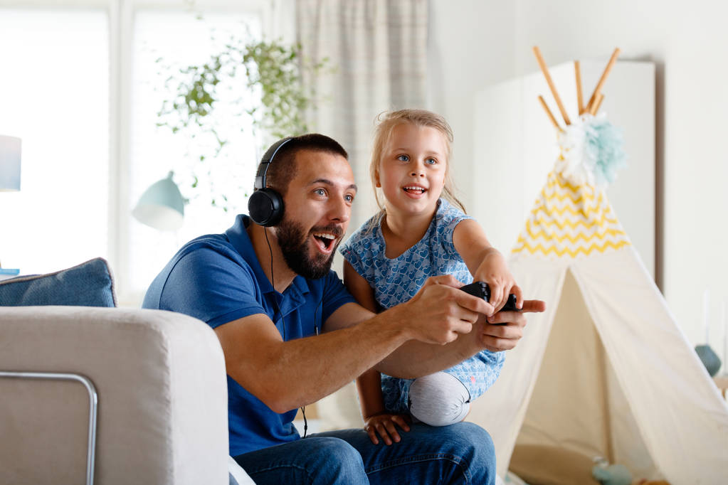 Giovane padre giocare ai videogiochi con la figlia insieme, seduto nel soggiorno del divano e divertirsi
.  - Foto, immagini