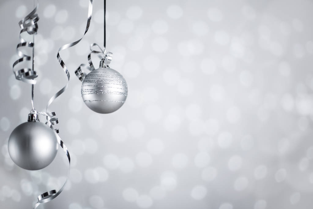 Silver Christmas new year balls with curly streamer ribbon bow over glittering bokeh lights background with copy space for text - Photo, Image