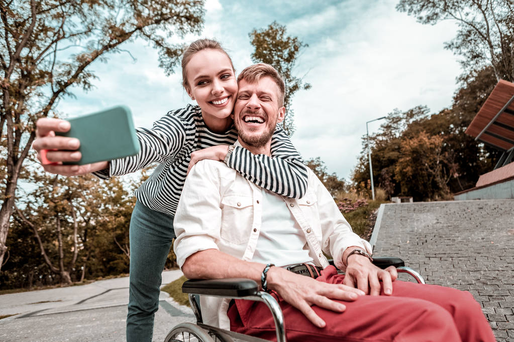 Man in rolstoel lachen terwijl leuke vriendin selfie mee te nemen - Foto, afbeelding