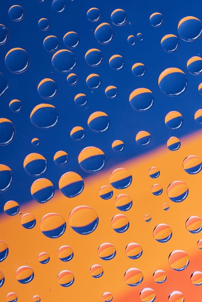 Nahaufnahme transparenter Wassertropfen auf blauem und orangefarbenem abstrakten Hintergrund - Foto, Bild