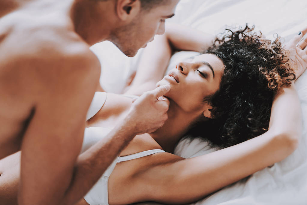 Mladý nádherný pár v prádle ležící na posteli. Pohledný muž dotýká Chin atraktivní ženy. Vášnivý romantický pár mít Sex doma. Vášeň, intimní vztah a lásku koncepce - Fotografie, Obrázek
