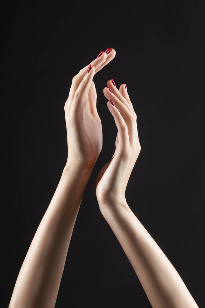 Close-up de belas mãos de mulher com manicure vermelho nas unhas. Creme para palmas, manicure e tratamento de beleza. Braços elegantes e graciosos com dedos finos e graciosos. Espaço para cópia. Isolado em preto
. - Foto, Imagem
