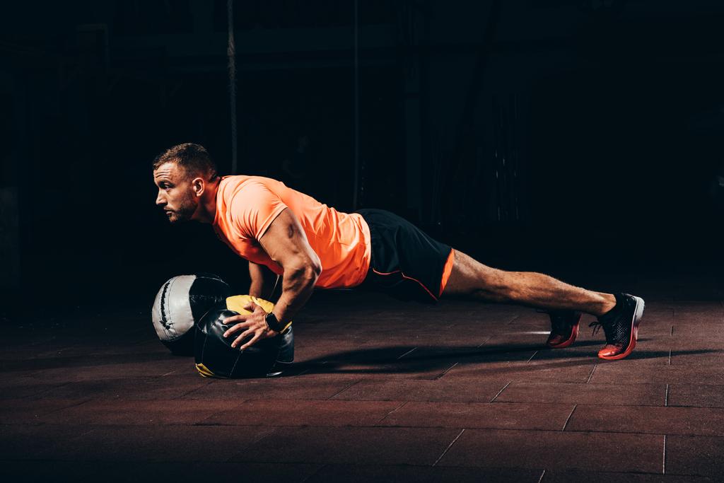 attraktiver athletischer Sportler macht Liegestütze auf Medizinball in dunkler Turnhalle - Foto, Bild