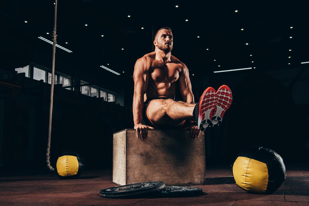 όμορφος αθλητικός άνδρας εκτέλεση όπλων ισορροπία στον κύβο στο σκοτεινό γυμναστήριο - Φωτογραφία, εικόνα