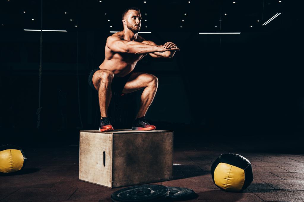 fisiculturista atlético bonito fazendo agachamentos no cubo no ginásio escuro
 - Foto, Imagem