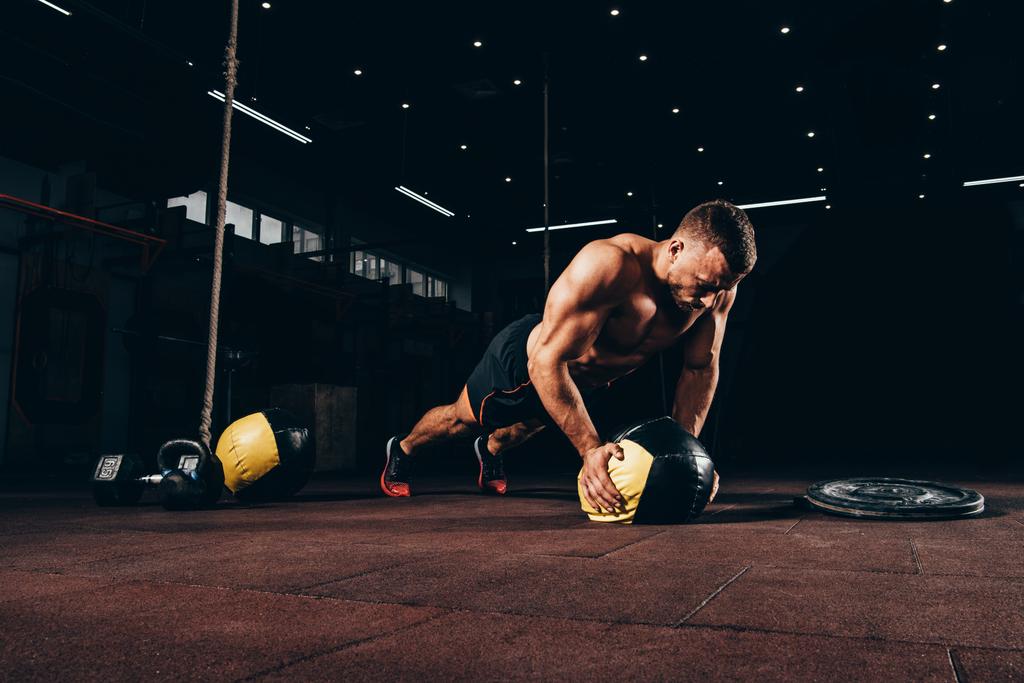 knappe fit sporter doet push ups op de bal van de geneeskunde in donkere sportschool - Foto, afbeelding